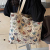 A beige corduroy tote bag decorated with floral accents and butterflies, held by a person.