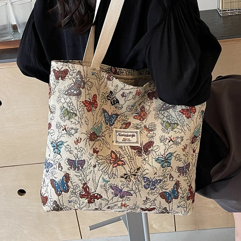 A beige corduroy tote bag decorated with floral accents and butterflies, held by a person.