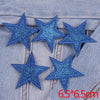 A set of five blue glitter star iron-on embroidered patches placed on a denim fabric.