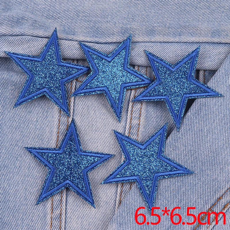 A set of five blue glitter star iron-on embroidered patches placed on a denim fabric.