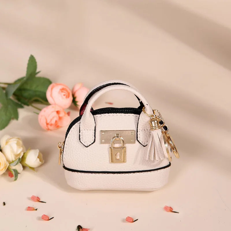 A white compact PU leather earbud case with a gold keychain is displayed on a light background.