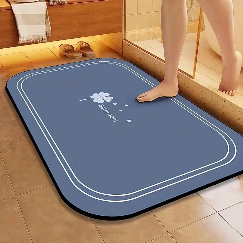A blue bathroom mat with a white outline and a small clover design is placed on a tiled floor.