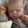 A newborn baby is sleeping, wrapped in a gray outfit and holding a white stuffed animal.