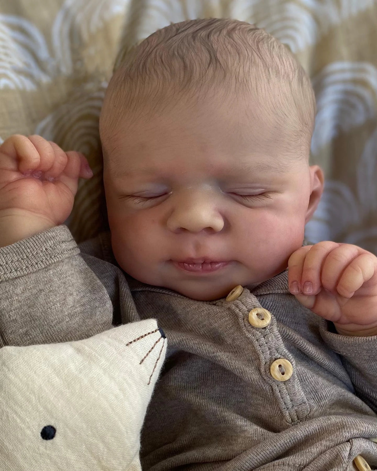 A newborn baby is sleeping, wrapped in a gray outfit and holding a white stuffed animal.