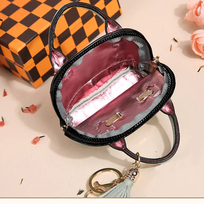 A black PU leather compact earbud case with a pink gradient lining and a gold-toned keychain is shown on a light background.