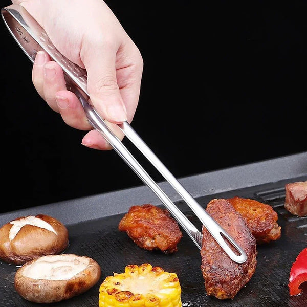 A hand holds heavy duty stainless steel kitchen tongs used for grilling or serving food.
