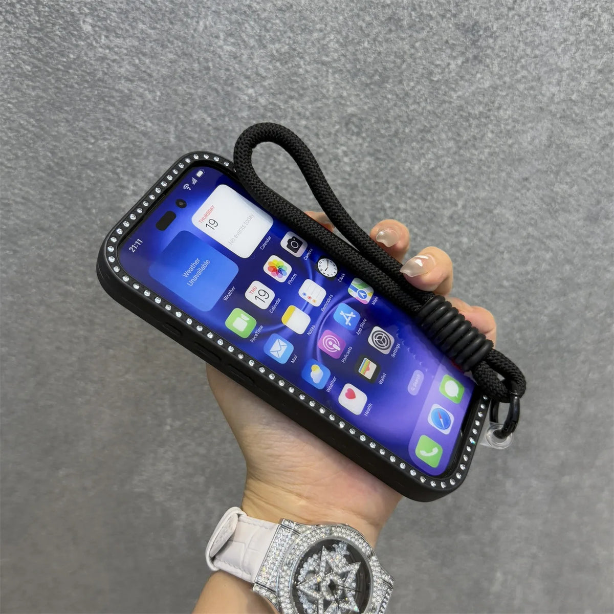 Una mano sostiene un smartphone en una funda transparente con correa negra en una pantalla gris.