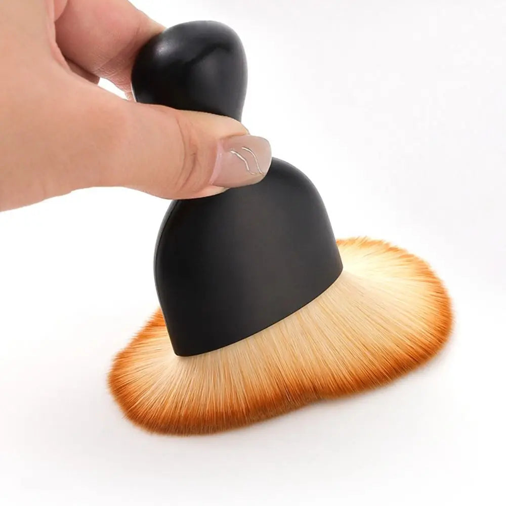 A hand is holding a black ultra-soft curved detailing brush with golden bristles.