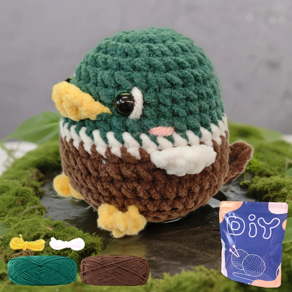 A finished green and brown crochet animal amigurumi next to yarn and a purple DIY kit bag.
