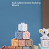 A stack of 12 soft silicone Jenga-style building blocks in various pastel colors on a wooden surface.