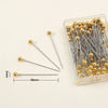 A clear container holds a pack of 100 gold-colored precision quilting pins with silver needles.