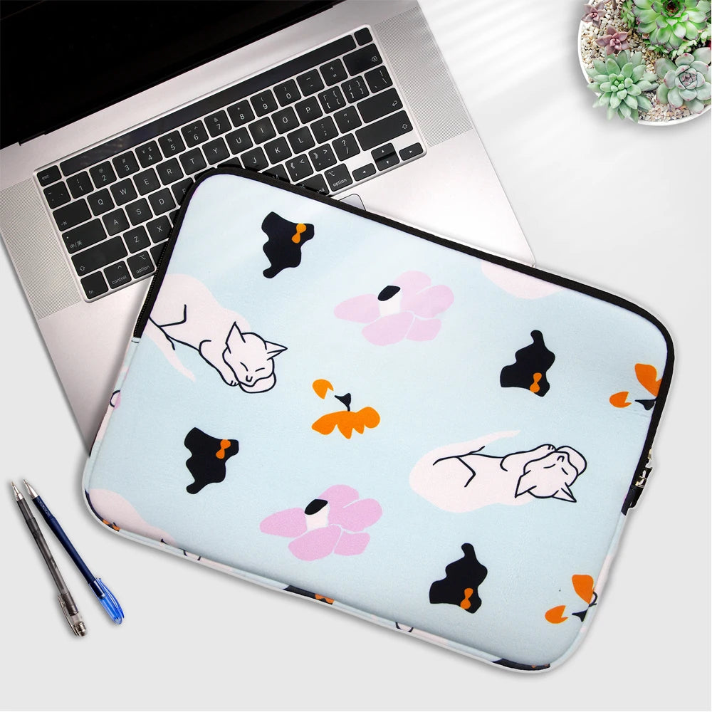 A light blue laptop sleeve featuring watercolor illustrations of cats and flowers, placed next to a silver laptop.