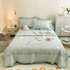 A light mint green embroidered floral quilted bedspread set displayed on a bed with white linens and bedside tables.