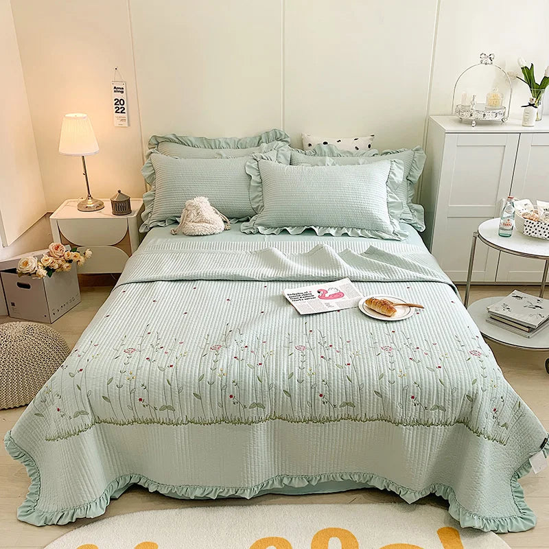 A light mint green embroidered floral quilted bedspread set displayed on a bed with white linens and bedside tables.
