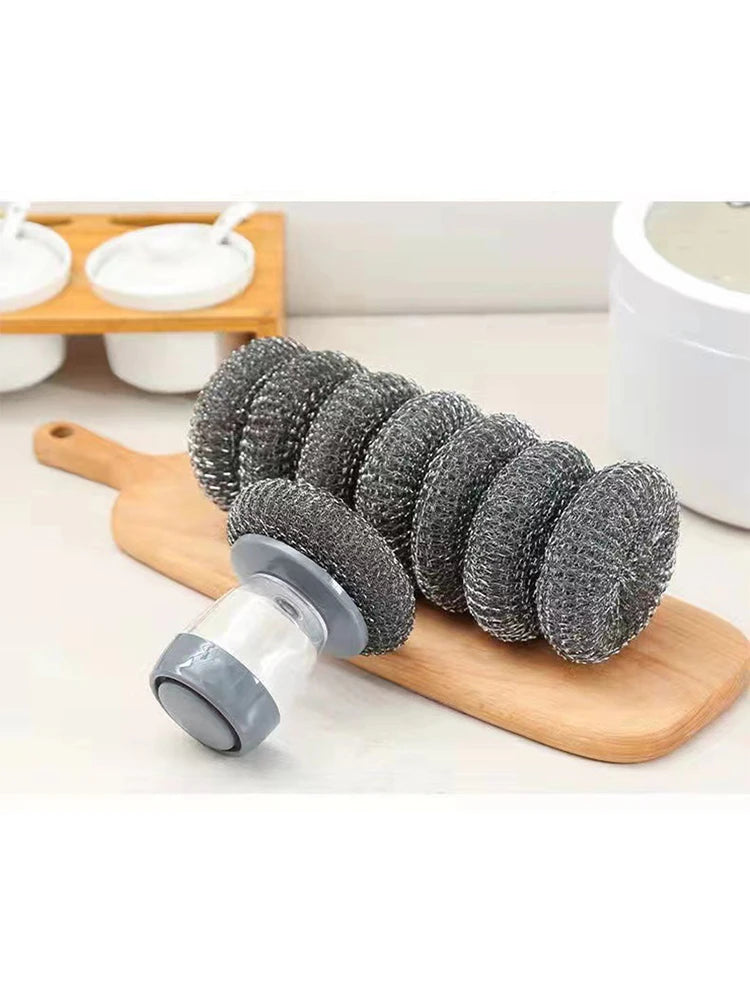 A set of grey press dish brushes with built-in soap dispensers displayed on a wooden board.