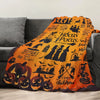 An orange Halloween themed flannel throw blanket featuring spooky silhouettes and bats draped over a gray sofa.