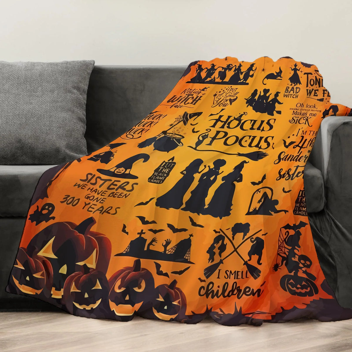 An orange Halloween themed flannel throw blanket featuring spooky silhouettes and bats draped over a gray sofa.