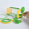 A yellow plastic insect observation cage with a net and a green magnifying glass is shown next to a hand.