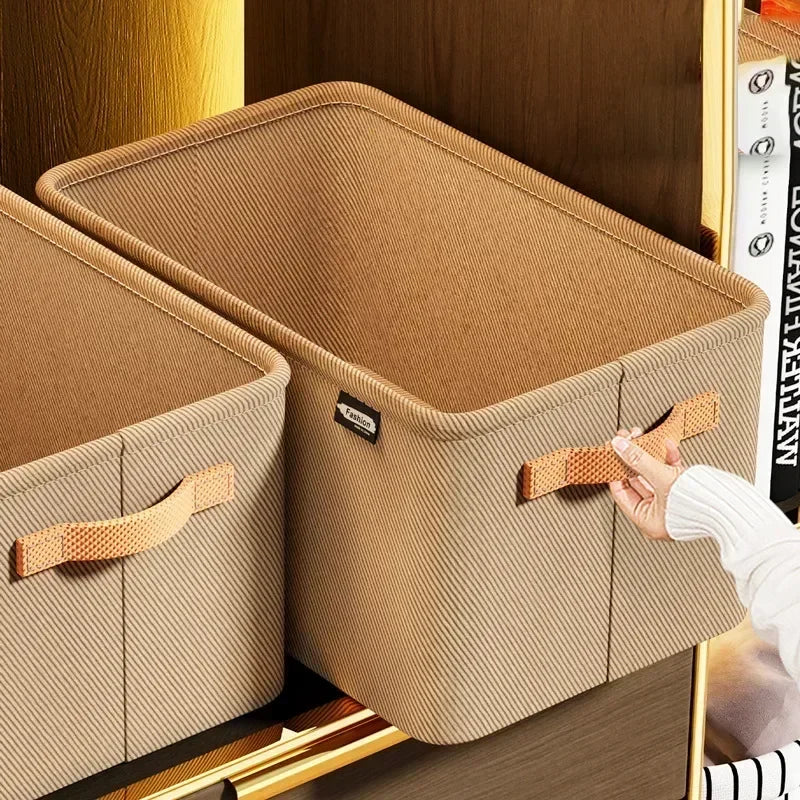 A light brown foldable fabric storage box is shown open, with a hand pulling out the lid.