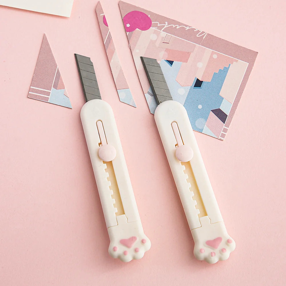 Zwei weiße, portable Katzenkrallenwerkzeuge mit grauen Klingen auf rosa Hintergrund neben gemustertem Papier.