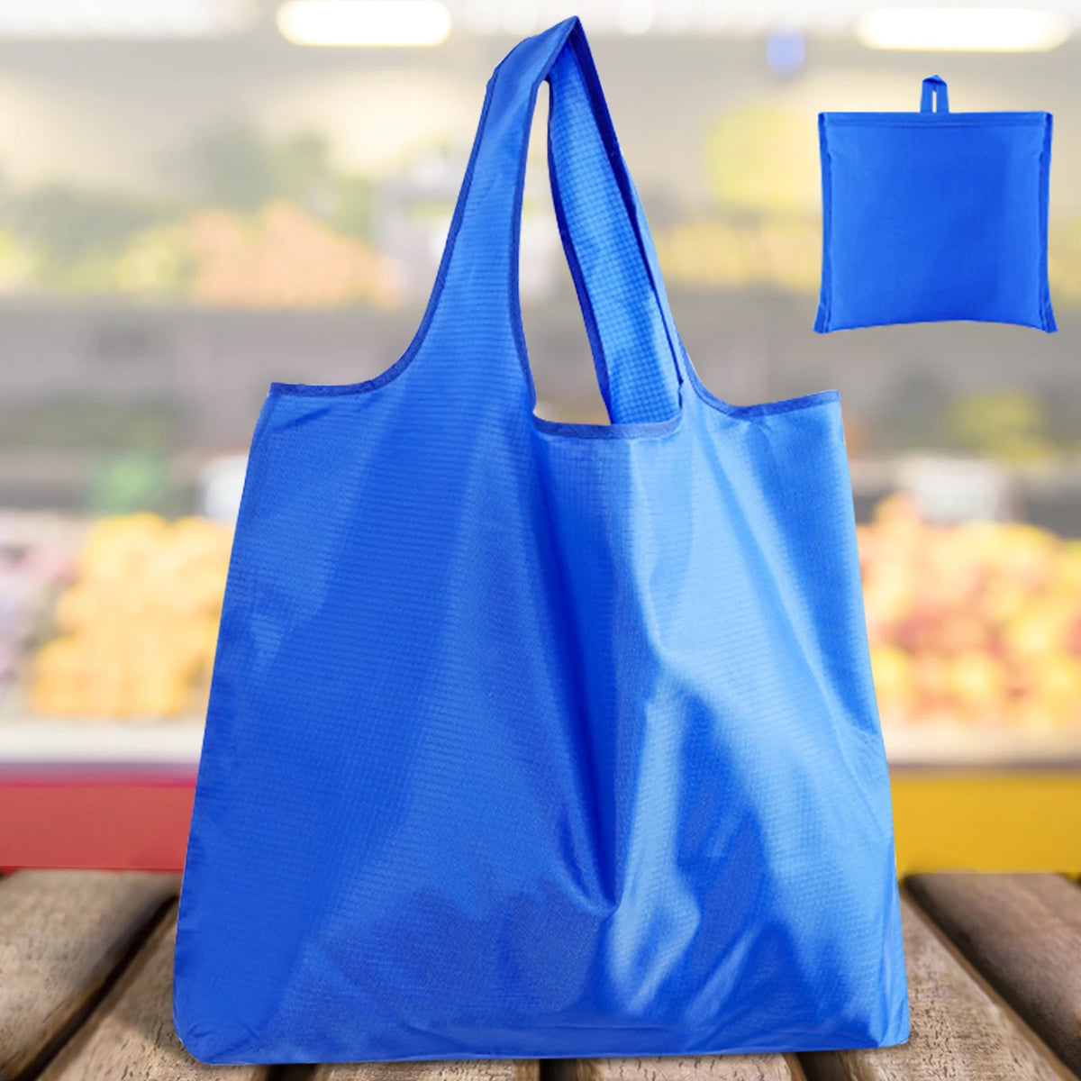 A bright blue foldable reusable grocery bag is shown against a blurred background of groceries.