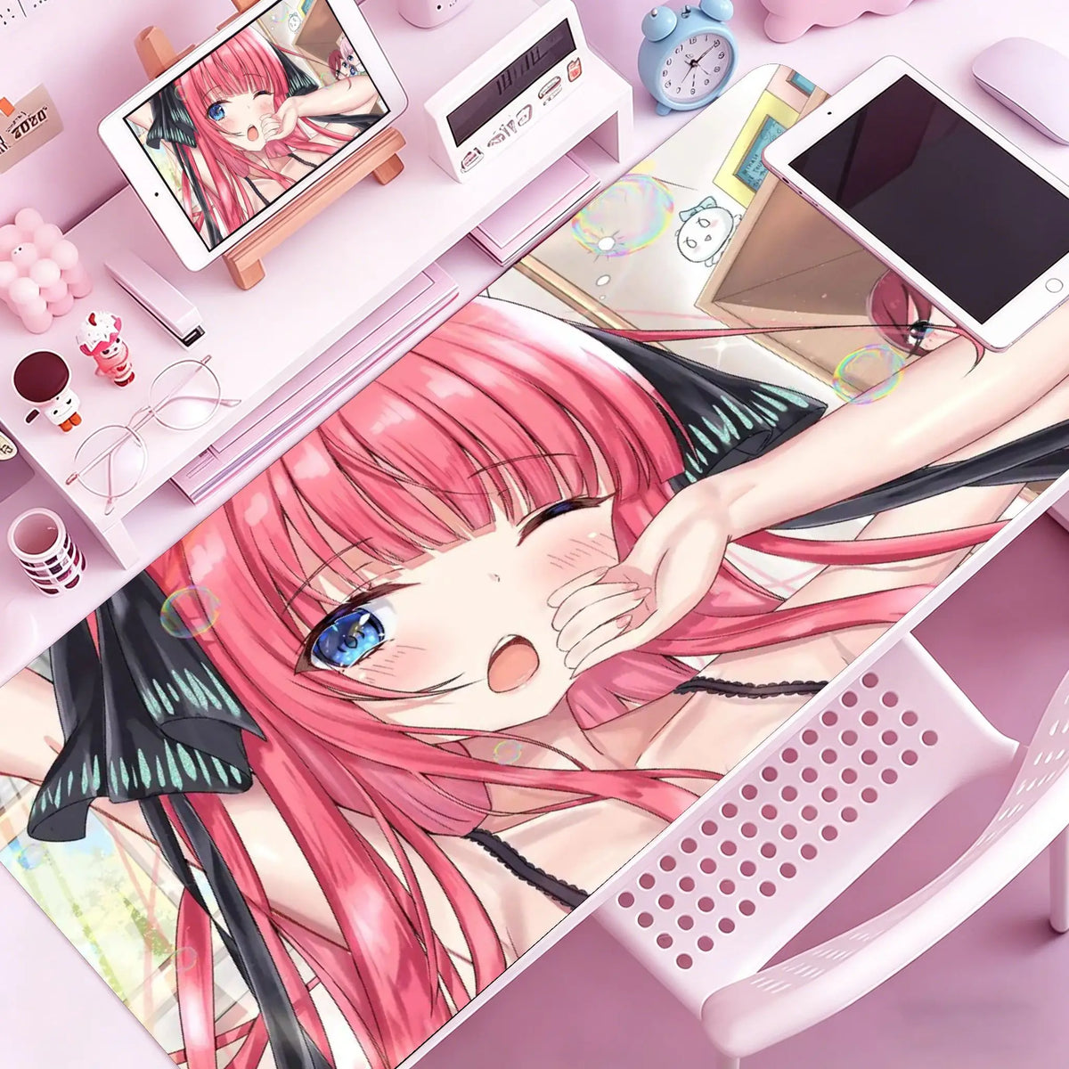 A close-up of a pink-haired anime character illustration on a mouse pad or desk mat, surrounded by stationery and gadgets.