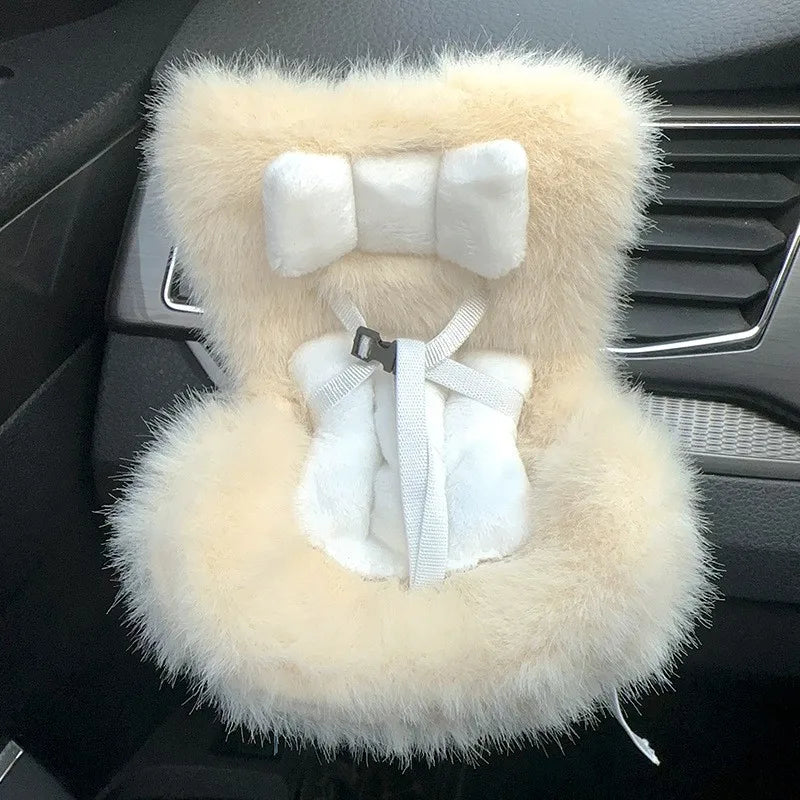 A fluffy beige and white miniature doll seat car vent decoration with a strap detail.
