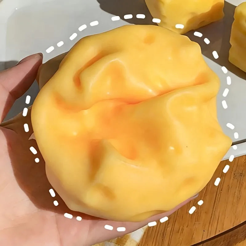 A hand holds a large, smooth, yellow squeeze playful cheese fidget toy against a white background.