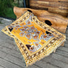 A yellow and orange bohemian jacquard woven throw blanket draped over a large wooden log outdoors.