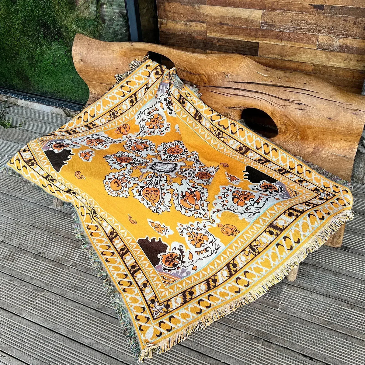 A yellow and orange bohemian jacquard woven throw blanket draped over a large wooden log outdoors.