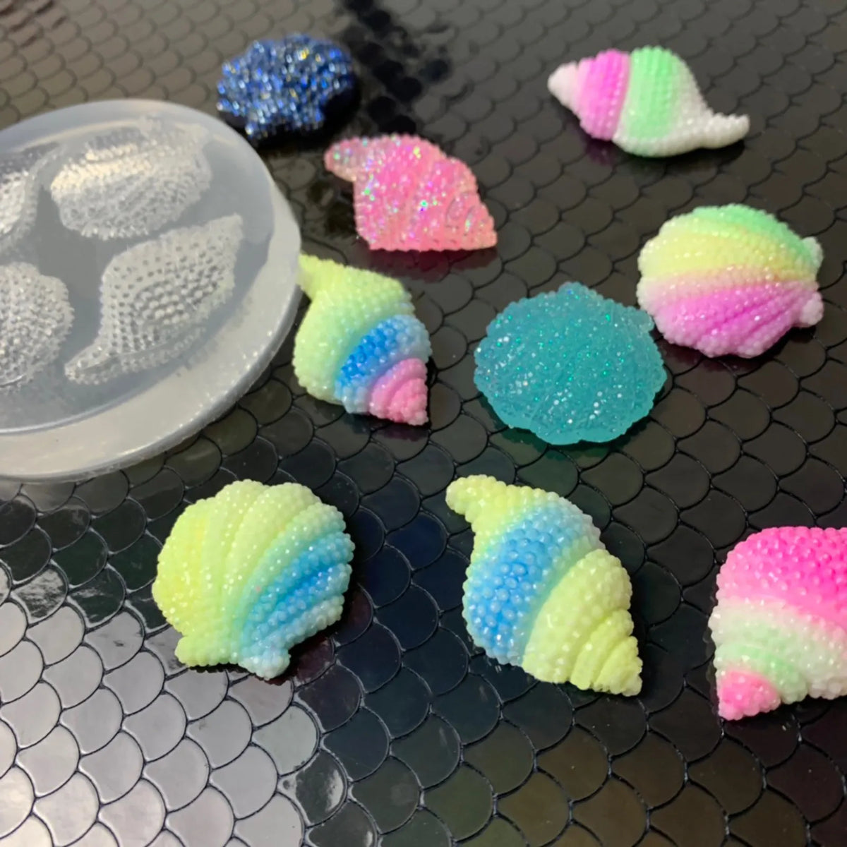 A collection of colorful fondant shells and starfish shapes in various shades including pink, green, blue, and purple on a da