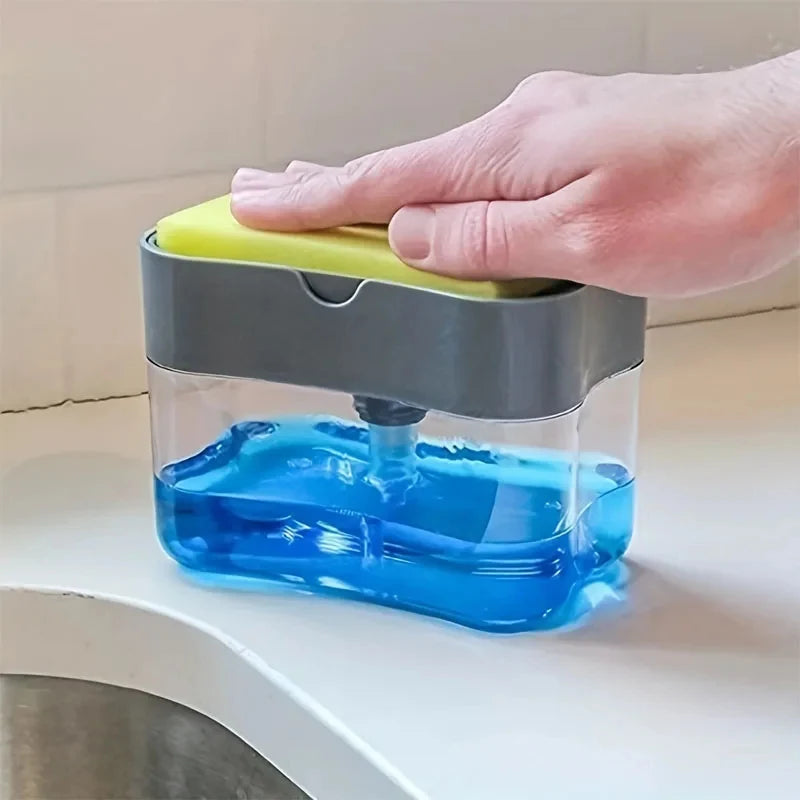 A hand is holding a clear soap dispenser with a gray lid and a yellow sponge holder, filled with blue liquid.
