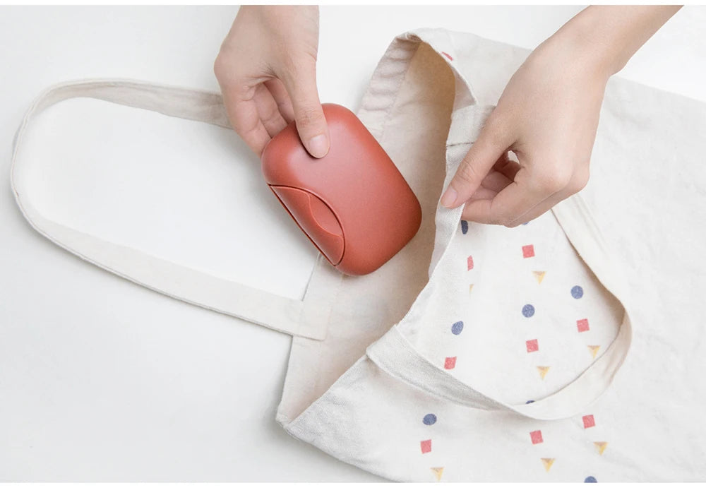 Hands place a compact, reddish-brown leak-proof travel soap box into a light-colored fabric pouch.