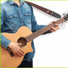 A person holds a brown acoustic guitar with a vintage cross pattern strap and pick pocket.