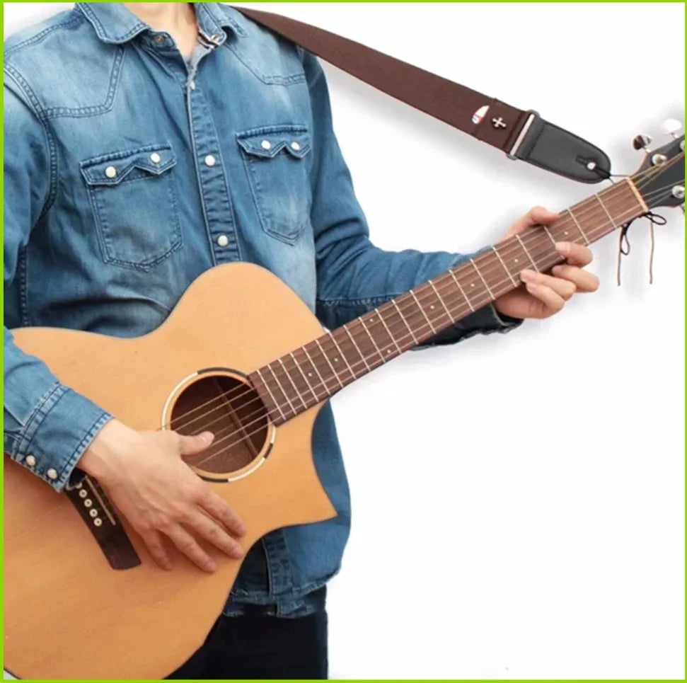 A person holds a brown acoustic guitar with a vintage cross pattern strap and pick pocket.