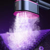A handheld garment steamer emits a cloud of steam over purple fabric.