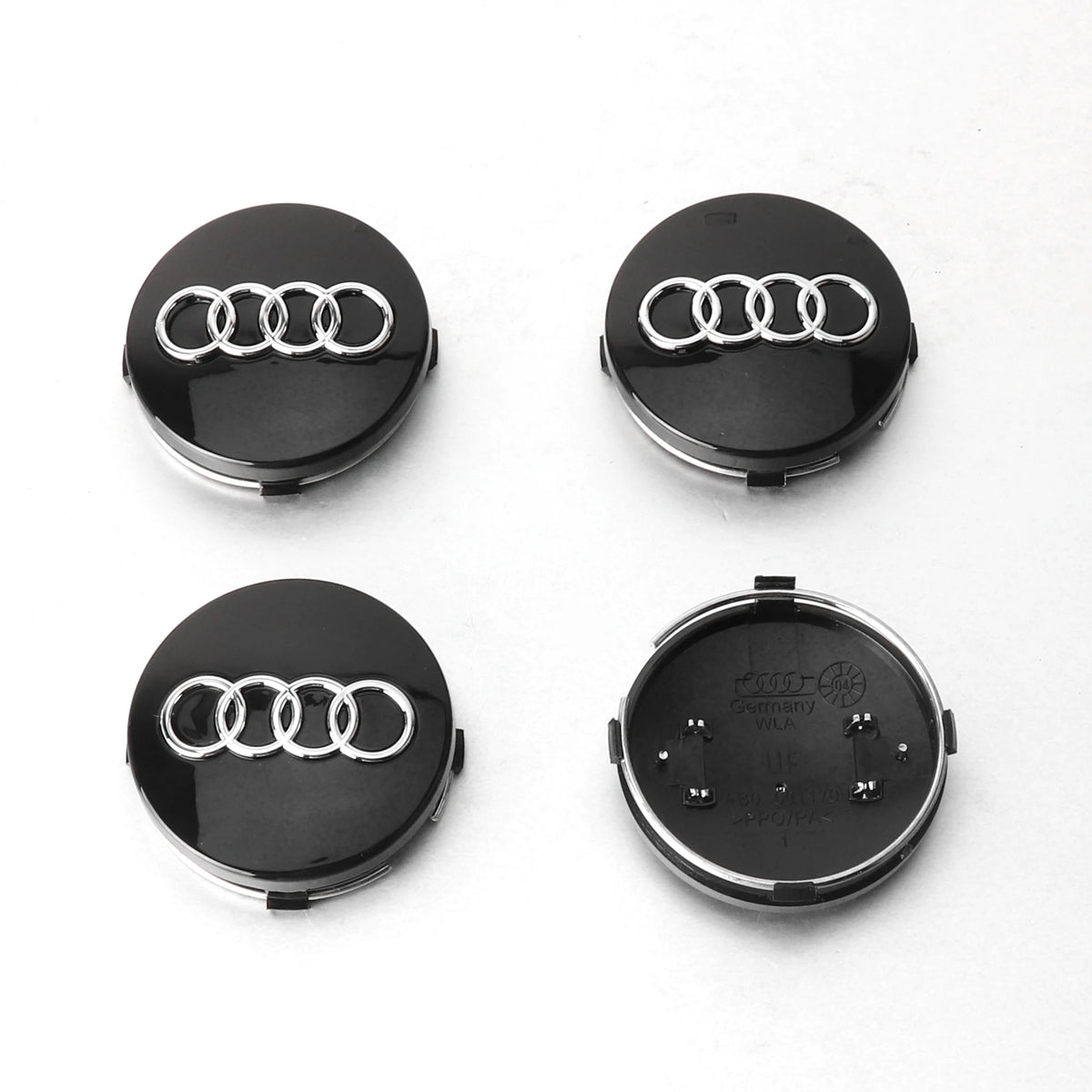 Four views of black decorative wheel covers with Audi rings on a white background.