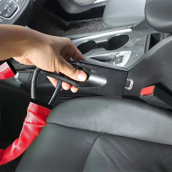 A hand is shown engaging a universal steering wheel lock with a seatbelt anchor mechanism in a car interior.