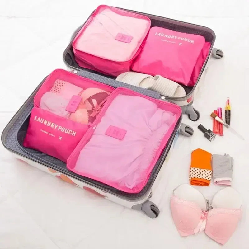 A set of six pink and lavender laundry pouches and packing cubes are displayed in a gray travel case.