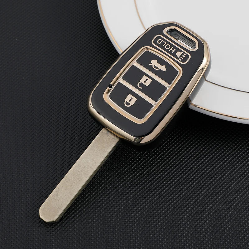 A black and gold TPU key fob cover with a metal blade is shown resting on a white surface.
