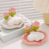 A pink tulip drainage soap dish with a white cloud-shaped soap is displayed on a light surface.