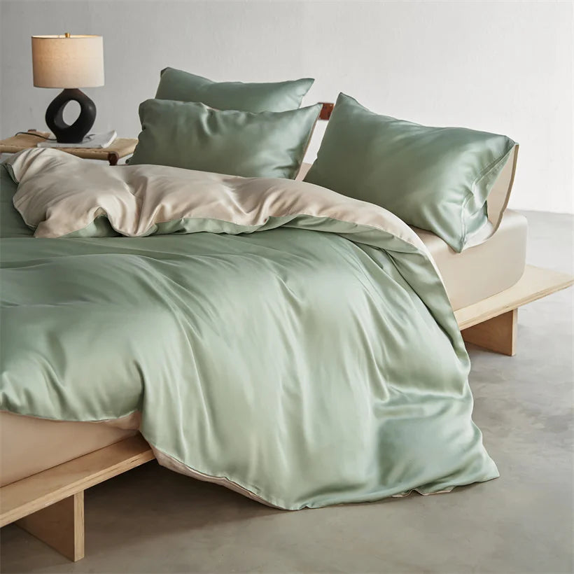 A light sage green luxury mulberry silk duvet cover set on a bed with natural wood accents and a lamp.