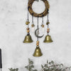A rustic witch bells door hanger wind chime made of woven branches and brass bells hanging against a light gray wall.