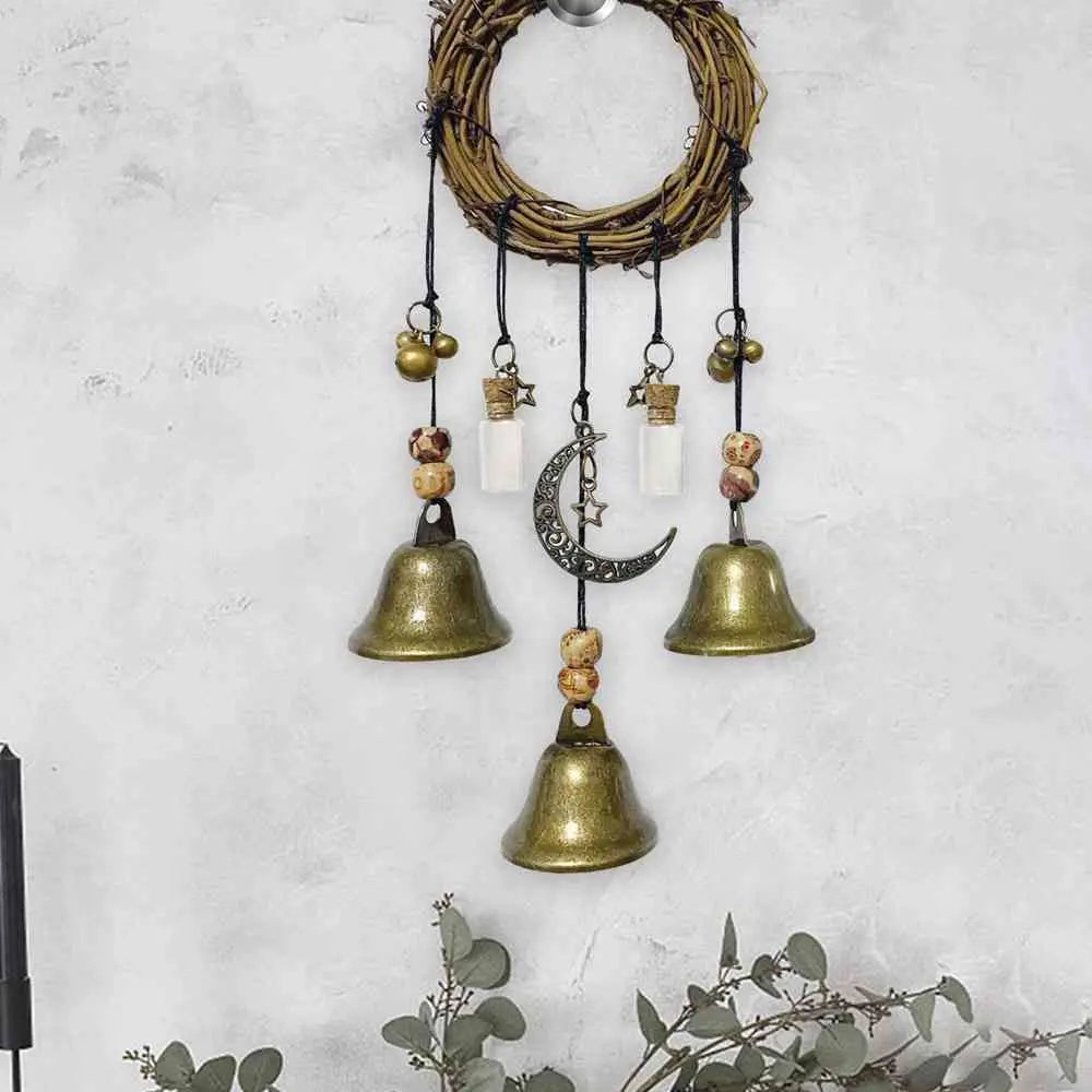 A rustic witch bells door hanger wind chime made of woven branches and brass bells hanging against a light gray wall.