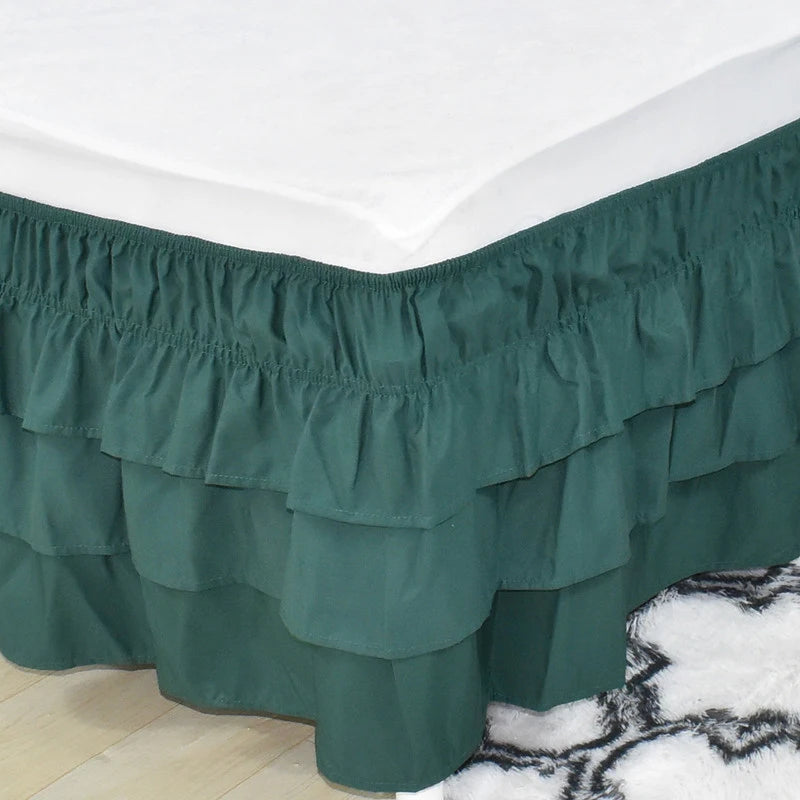 A dark green adjustable elastic bed skirt with ruffled layers covering the bottom of a mattress.