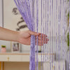 A hand is pulling a long, purple tassel string curtain down, showing the delicate strands and texture.