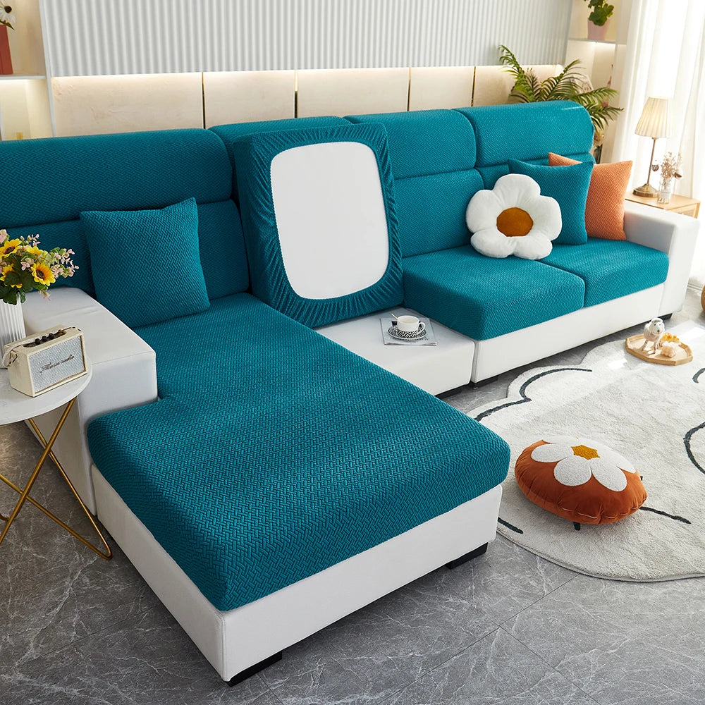 A teal sofa slipcover with white accents and decorative pillows is shown in a bright living room setting.