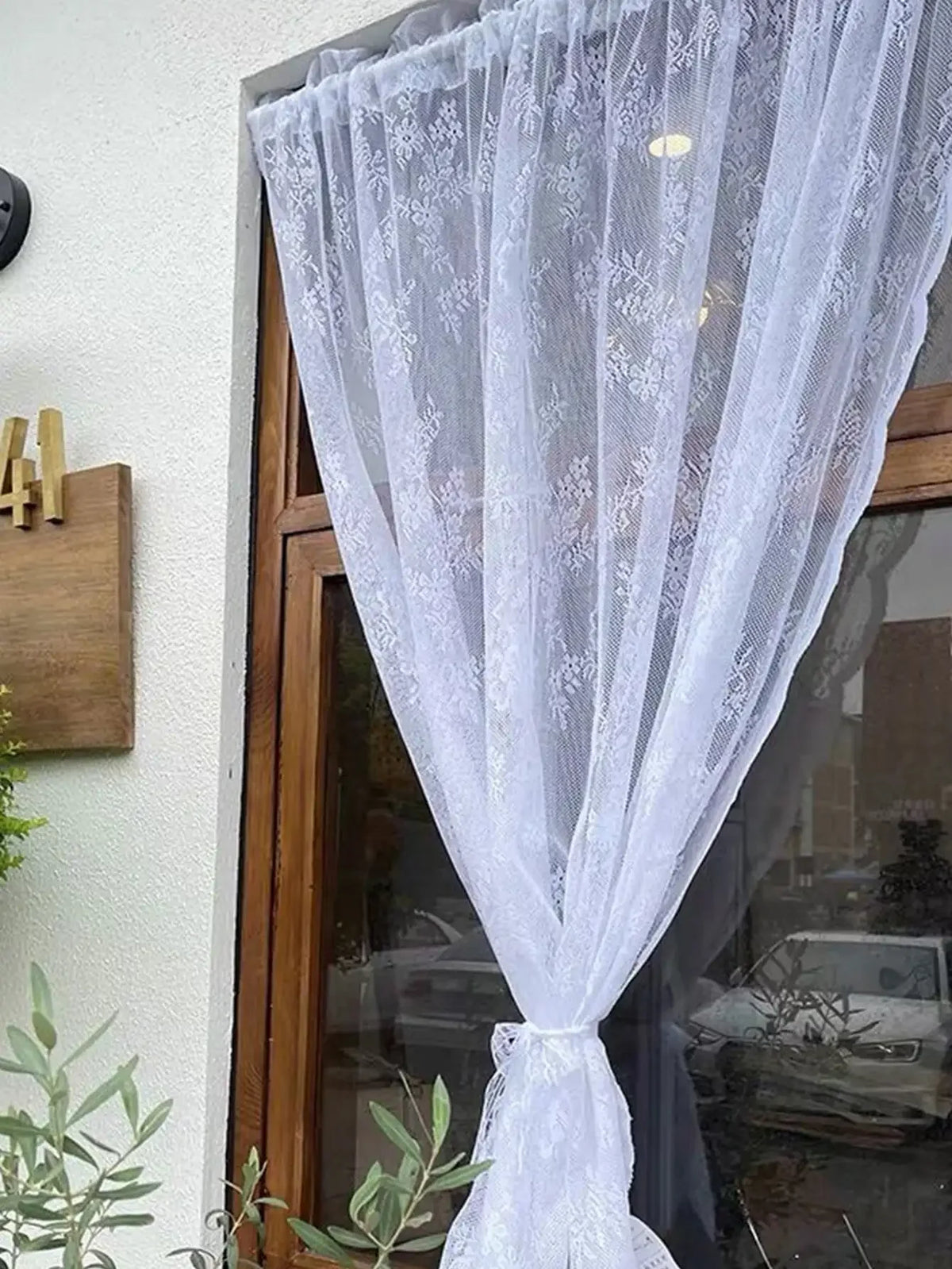 Un rideau blanc transparent avec broderie florale drapé dans un cadre de fenêtre.