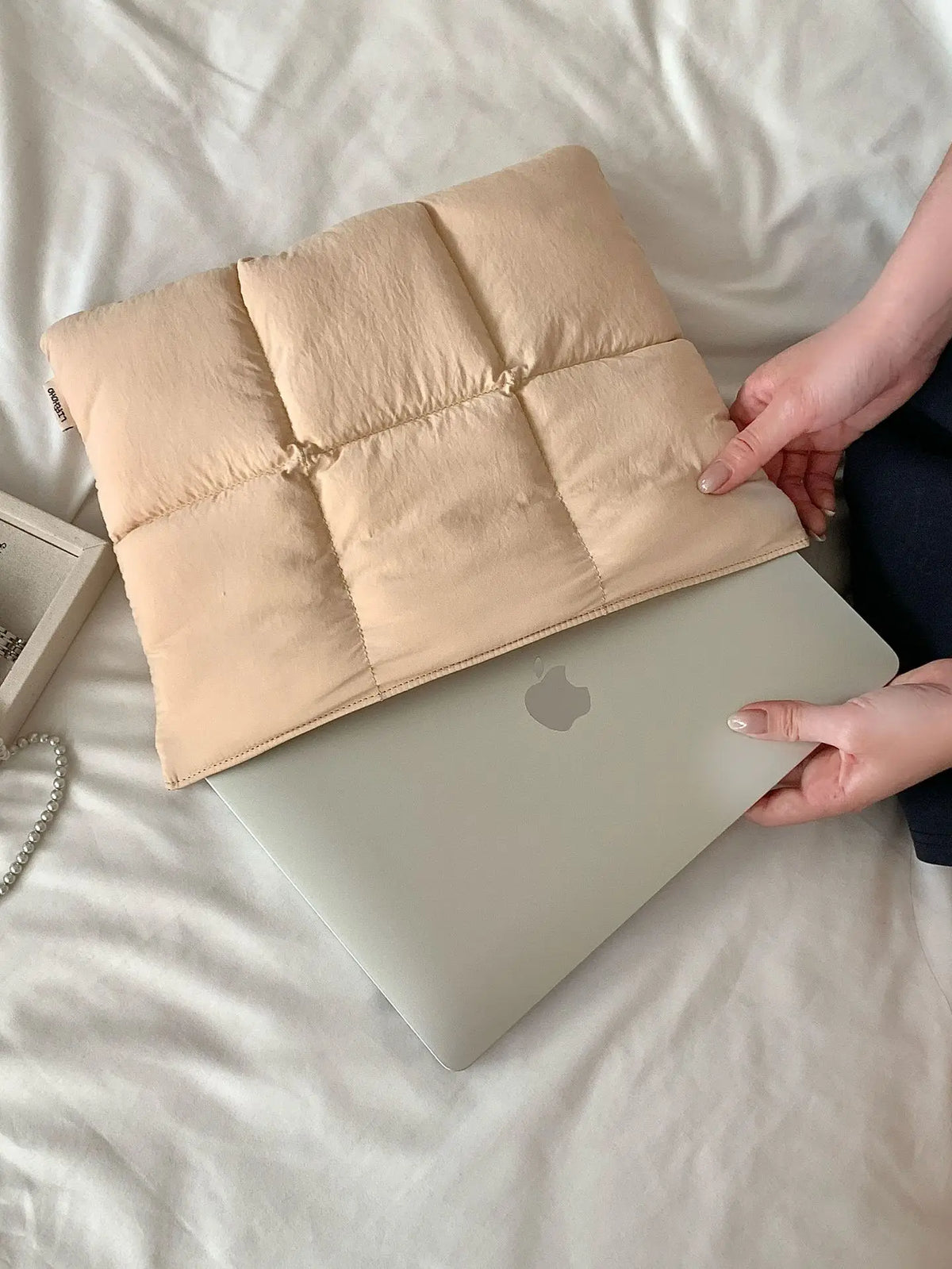 Hülle für Laptop aus beiger gesteppter Daunenjacke auf silbernem Laptop in heller Bettwäsche