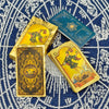 A set of gold foil tarot cards and a guidebook are displayed on a blue patterned fabric.